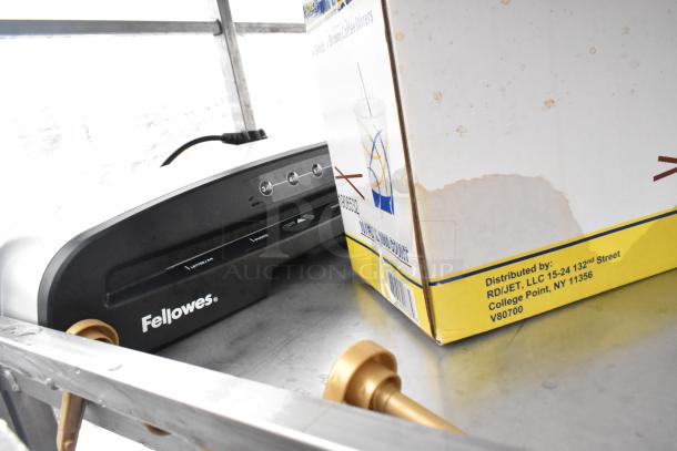 Chrome shelving unit with contents including a Fellowes laminator and a box of stirrers. Buyer must dismantle.