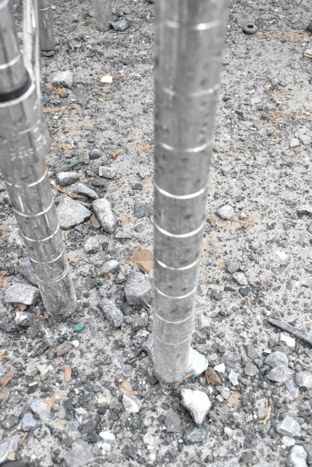 Chrome finish 3-tier wire shelving unit leg on gravel surface, displaying wear and sturdy construction. Buyer to dismantle.
