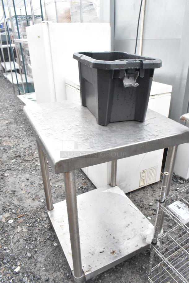 Stainless steel table with under shelf, used condition, located outdoors. Durable construction, ideal for storage or kitchen use.