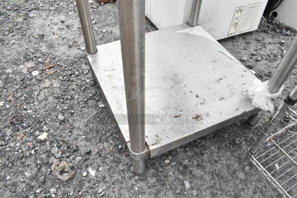 Stainless steel table with an under shelf, shows signs of wear, sturdy legs, suitable for kitchen or industrial use.