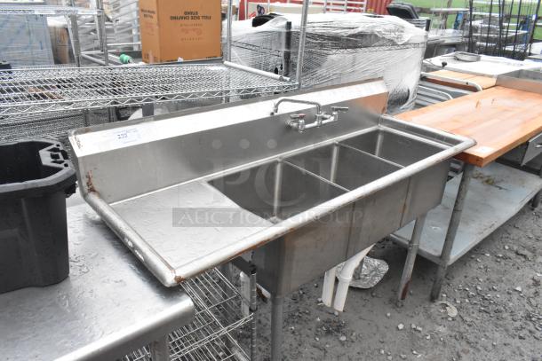 Stainless steel 3-bay sink with left side drain board, faucet, and handles. Features sturdy legs and integrated backsplash.