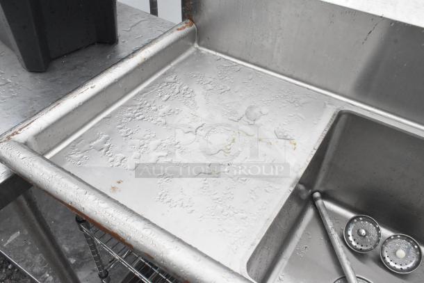 Stainless steel 3 bay sink with left side drain board, faucet, and handles; some surface wear visible.