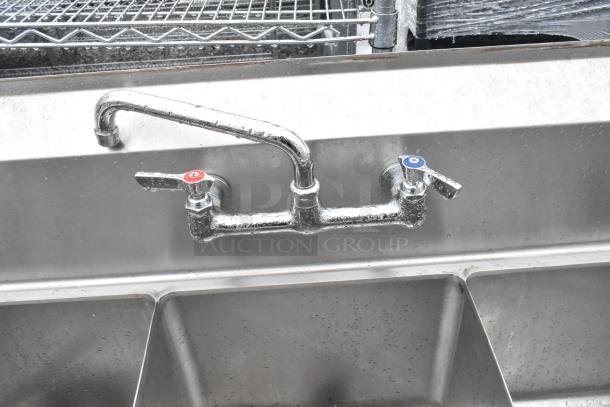 Stainless steel 3 bay sink with left side drain board, dual-handle faucet, and visible water droplets on the surface.