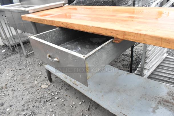 Butcher block table with metal drawer and under shelf, wood top, industrial style, visible wear, ideal for kitchen use.