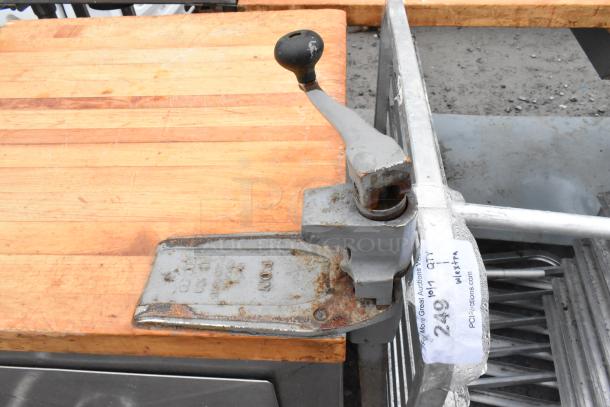 Metal commercial counter with butcher block countertop, mounted can opener, two drawers. Visible wear and commercial use.