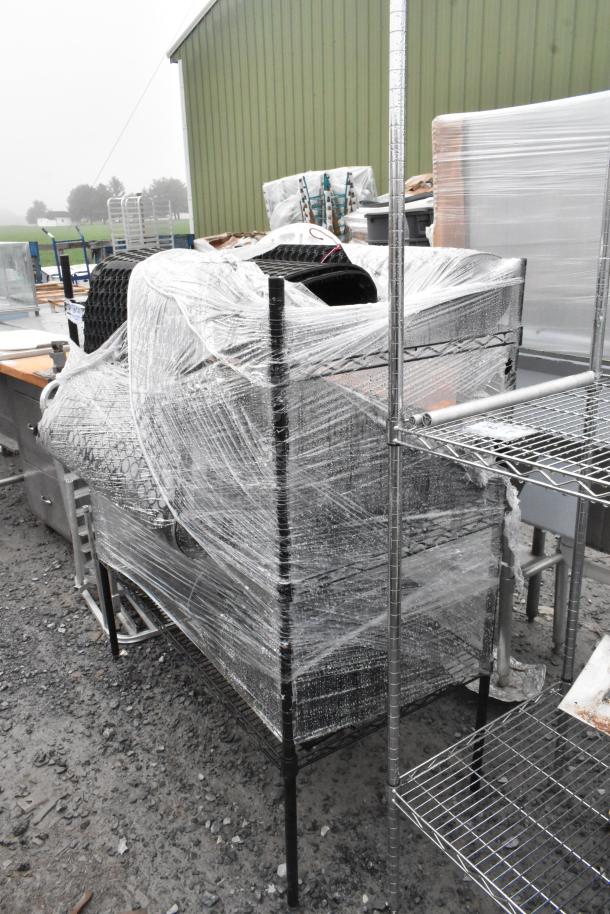 Black 3-tier wire shelving unit with contents, wrapped in plastic for shipping. Includes floor mat. Buyer must dismantle.