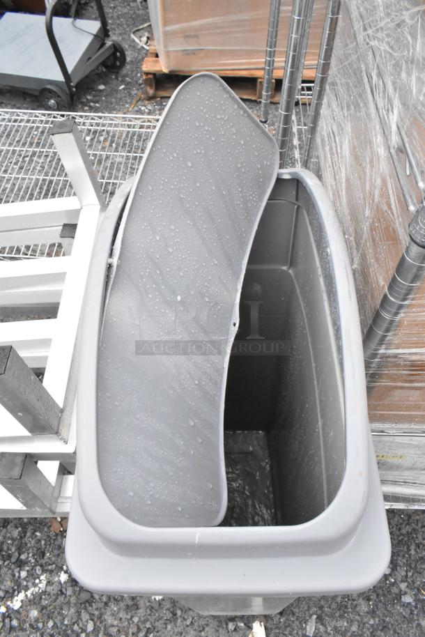 Gray Poly Slim Jim trash can, open lid, rectangular shape, outdoor setting, wet surface, good condition.