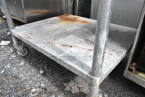 Stainless steel equipment stand with metal under shelf on commercial casters, visible rust and wear on surface.