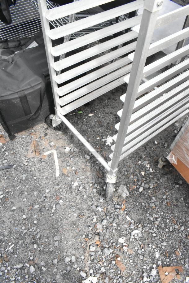 Metal pan transport rack with multiple shelves on commercial casters, shown in used condition, suitable for kitchen use.