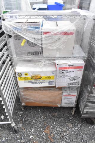 Chrome finish wire shelving unit on commercial casters, filled with boxed contents, wrapped in plastic. Buyer must dismantle.