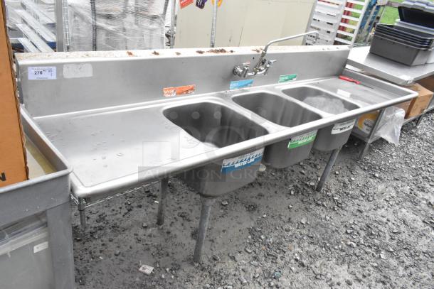 Stainless steel 3 bay sink with dual drain boards and faucet, showing wear and rust spots, labels for waste, rinse, sanitize.