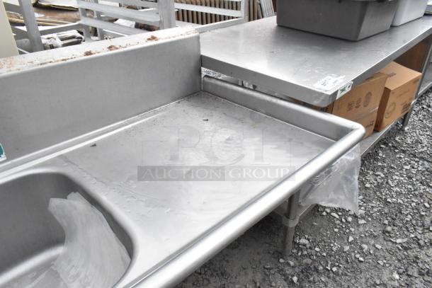 Stainless steel 3 bay sink with dual drain boards, faucet, and handles, showing wear and surface stains, suitable for heavy-duty use.