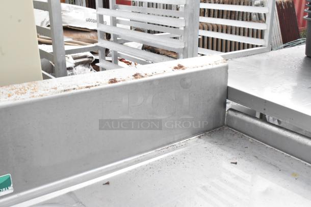 Stainless steel 3 bay sink with dual drain boards, faucet, and handles. Visible rust and dirt indicate used condition.