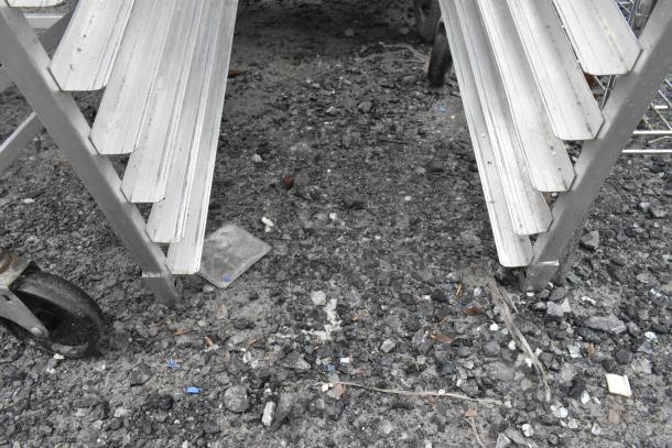 2 metal pan transport racks with slotted shelves on commercial casters, in used condition, outdoors.
