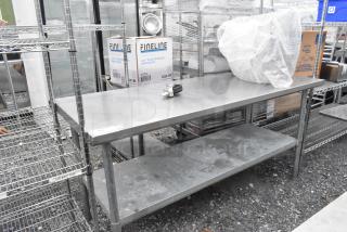Stainless steel table with metal under shelf, slight wear, ideal for kitchen or restaurant use. Durable and functional.