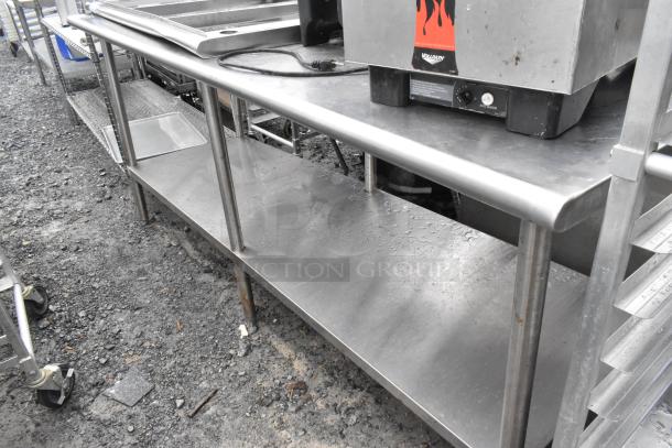 Stainless steel table with under shelf, industrial design, used condition, minor surface wear, suitable for kitchen or workshop use.