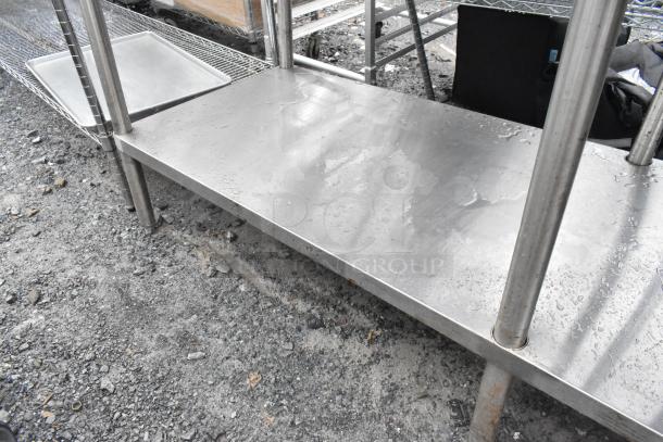 Stainless steel table with under shelf, wet surface, sturdy legs, minor rust spots, ideal for industrial use.