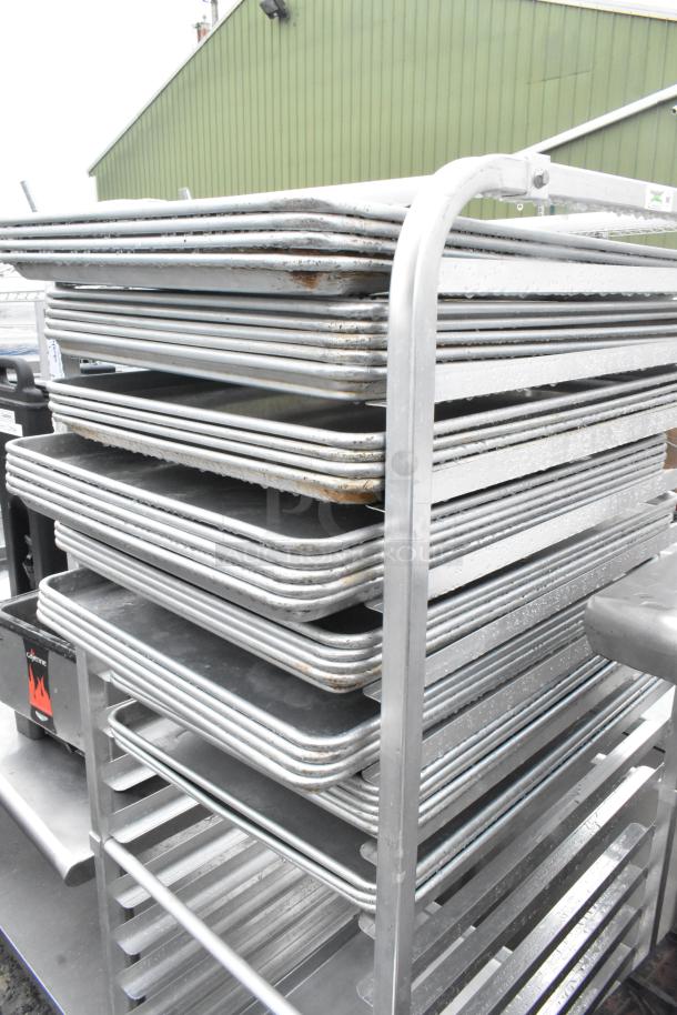 Metal transport pan rack on casters with 35 full-size baking pans, showing wear. Ideal for commercial use.