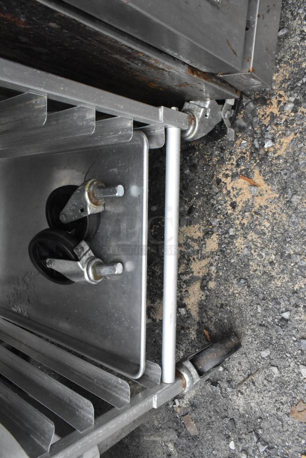 Metal transport pan rack with 35 full-size baking pans, commercial casters visible, shown on asphalt ground.