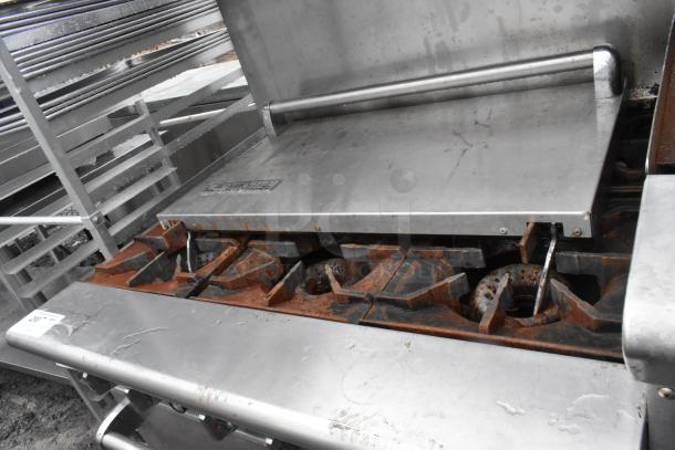 American Range stainless steel commercial gas-powered 6 burner range with right side flat top griddle, 2 ovens, over shelf, and backsplash. Visible rust on burners. Model tag intact.