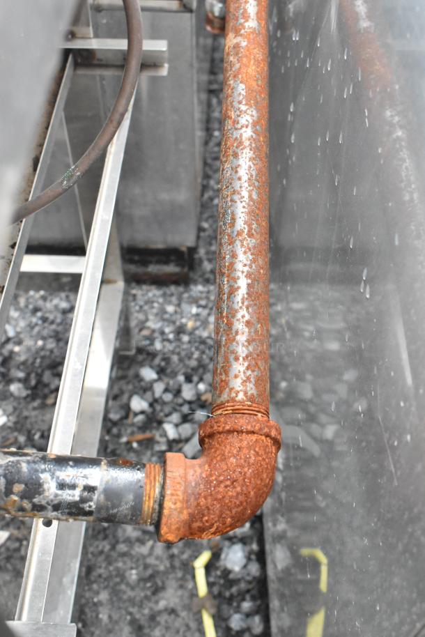 Rusted pipe close-up near a stainless steel commercial gas-powered 4 burner range on equipment stand.