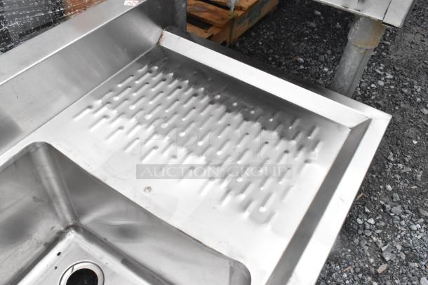 Regency 600B11014213 stainless steel back bar sink with dual drain boards, no legs, shown outdoors, minor wear visible.