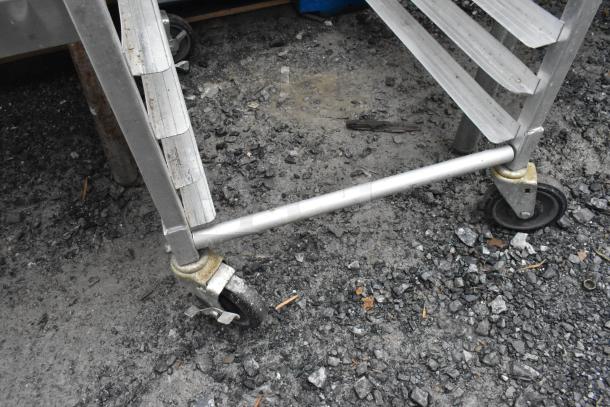 Metal commercial pan transport rack with sturdy commercial casters, shown outdoors on gravel. Suitable for high-capacity use.