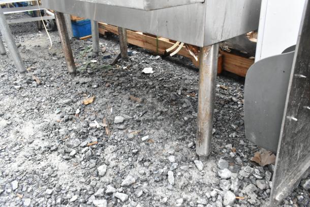 Stainless steel ice bin with speedwell and missing legs, used condition, set on gravel surface.