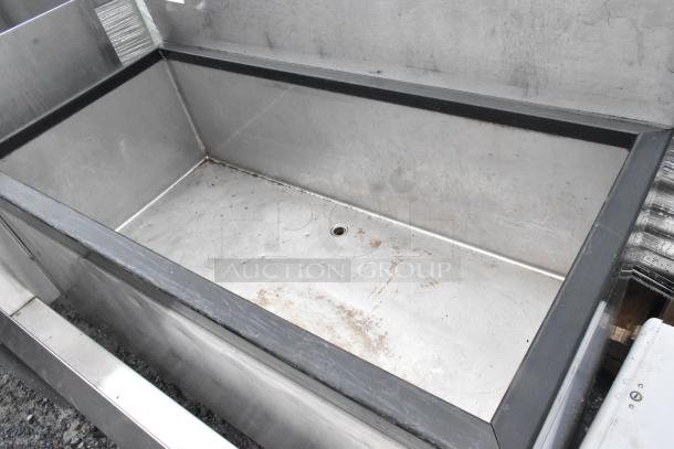 Stainless steel ice bin with speedwell, no legs. Features open top, drain hole, and signs of wear. Suitable for commercial use.
