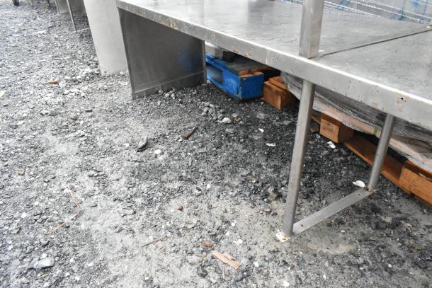 Stainless steel 2-tier over shelf, sturdy metal, visible wear and weathering, resting on pallets, suitable for storage.