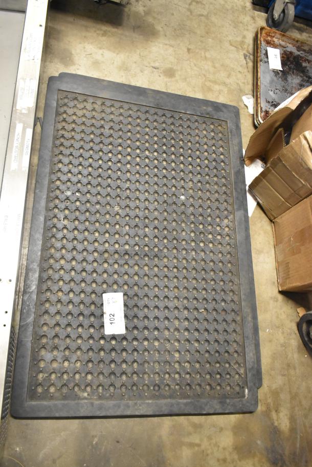 Black anti-fatigue floor mat with perforated design, rectangular shape, tagged with number 102, fair condition.
