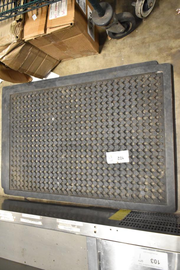Black anti-fatigue floor mat with textured surface, used condition. Tag number 102 visible.