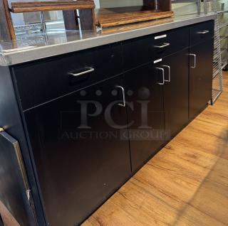 Metal top work station with black cabinets and drawers. Features silver handles and visible labels. In good condition.