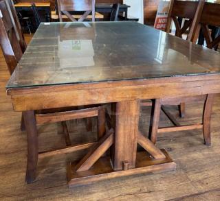 Wooden dining table with glass top, rectangular, sturdy base, rich brown finish, minor wear, suitable for elegant dining.