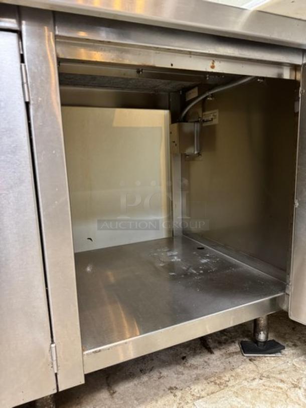 Stainless steel equipment stand with storage, featuring a sturdy frame and interior shelf. Signs of wear visible inside.