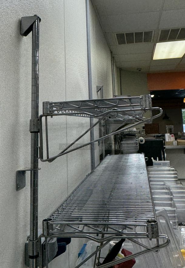 Stainless wire shelving mounted on a wall, featuring durable metal construction and adjustable brackets, in good condition.