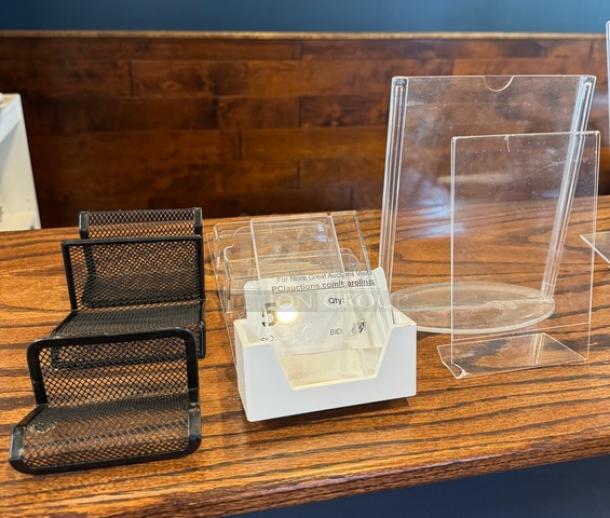 Assorted business card holders, including black mesh and clear acrylic designs, on wooden surface, in good condition.