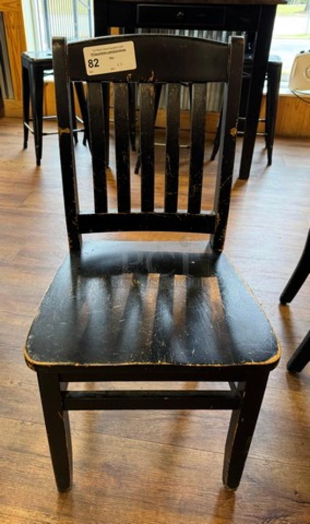 Black wooden dining chair with slatted back; visible wear and distressing. Included in set of four. Auction tag number 82.