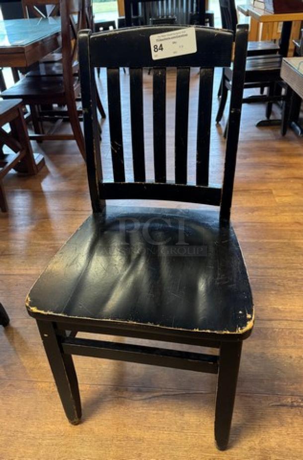 Black wooden dining chair with vertical slat back, visible wear on seat, auction tag "84" attached. Set of 4.