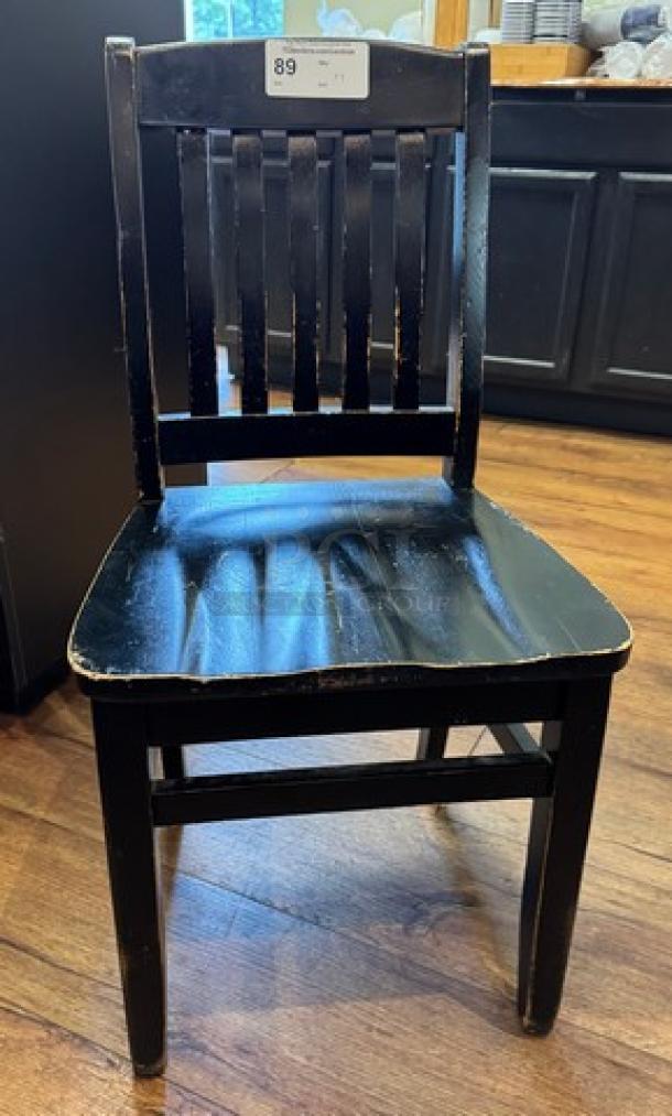 Black wooden dining chair with slatted back, distressed finish, and visible wear. Auction tag marked "89". Set of four.