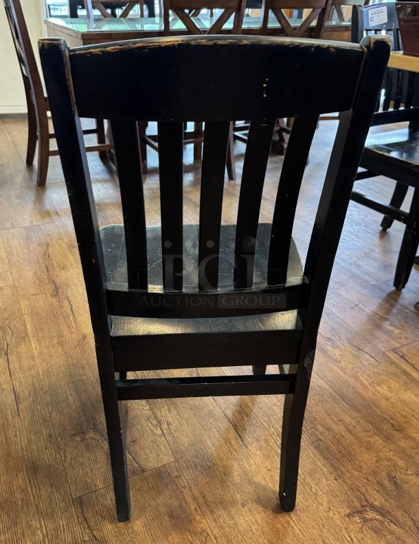Black wooden dining chair with slatted back, visible wear on edges, part of a set of four for auction.