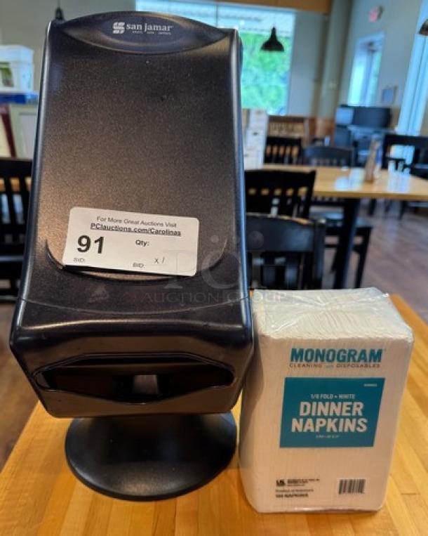 SanJamar tabletop napkin dispenser with Monogram dinner napkins, excellent condition, black finish, auction tag visible.