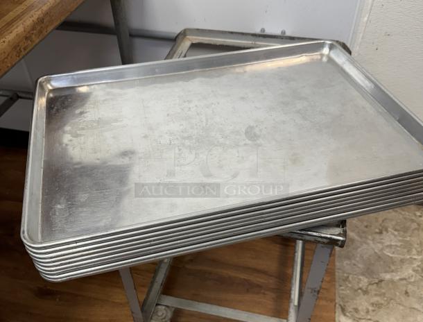 Full size sheet pans, stack of 10, used condition, durable aluminum, slight wear visible, ideal for commercial baking.