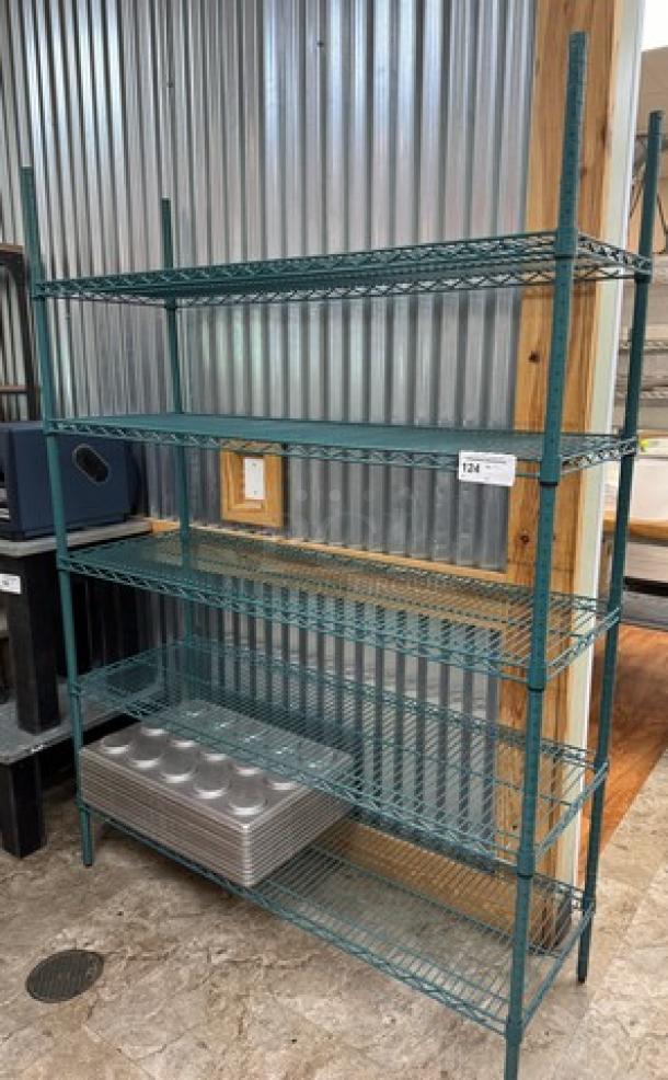 Wire rack with 5 sturdy metal shelves, green finish, standing against a corrugated metal wall. Ideal for storage.