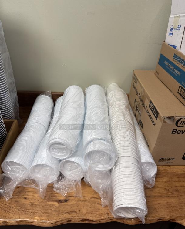 Assorted coffee items including take-out cups, lids, and stirrers in plastic packaging on a wooden surface.