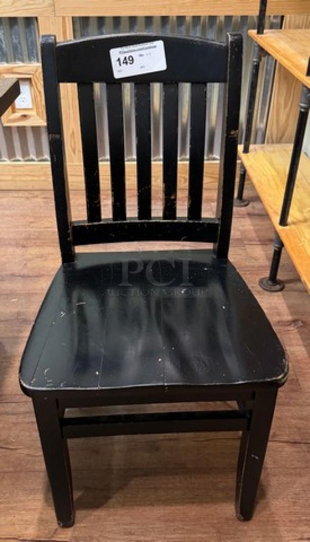 Black dining room chair with slatted backrest, wooden construction, visible wear. Auction tag marked "149." Set of 4.