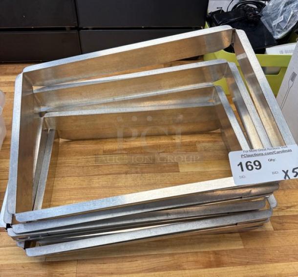 5 half-size sheet pan extenders, metal, stacked. Good condition. Auction tag indicates "Qty: 5, Bid: X".