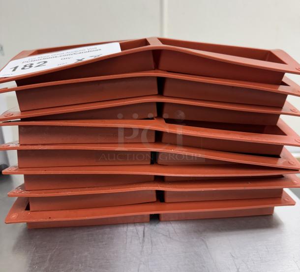 Stack of 8 red silicone baking molds. Each mold has 6 rectangular cavities. Slightly used condition. Auction lot tag visible.