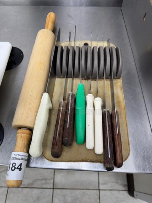 Wooden rolling pin 21" and knife holder with 8 assorted knives, various handle colors, on a metal kitchen surface.