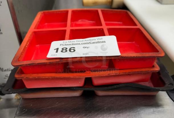 Red silicone baking molds, square compartments, stack of three, used condition, auction lot tag 186 visible.